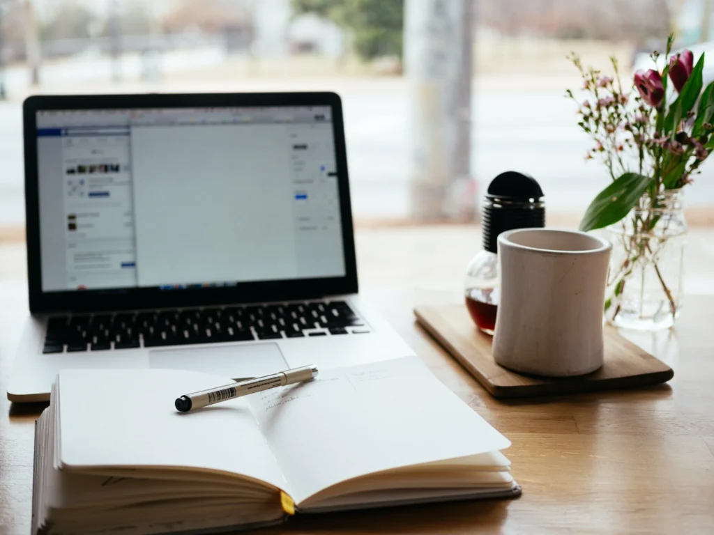 computer with a notebook and pen and warm coffee