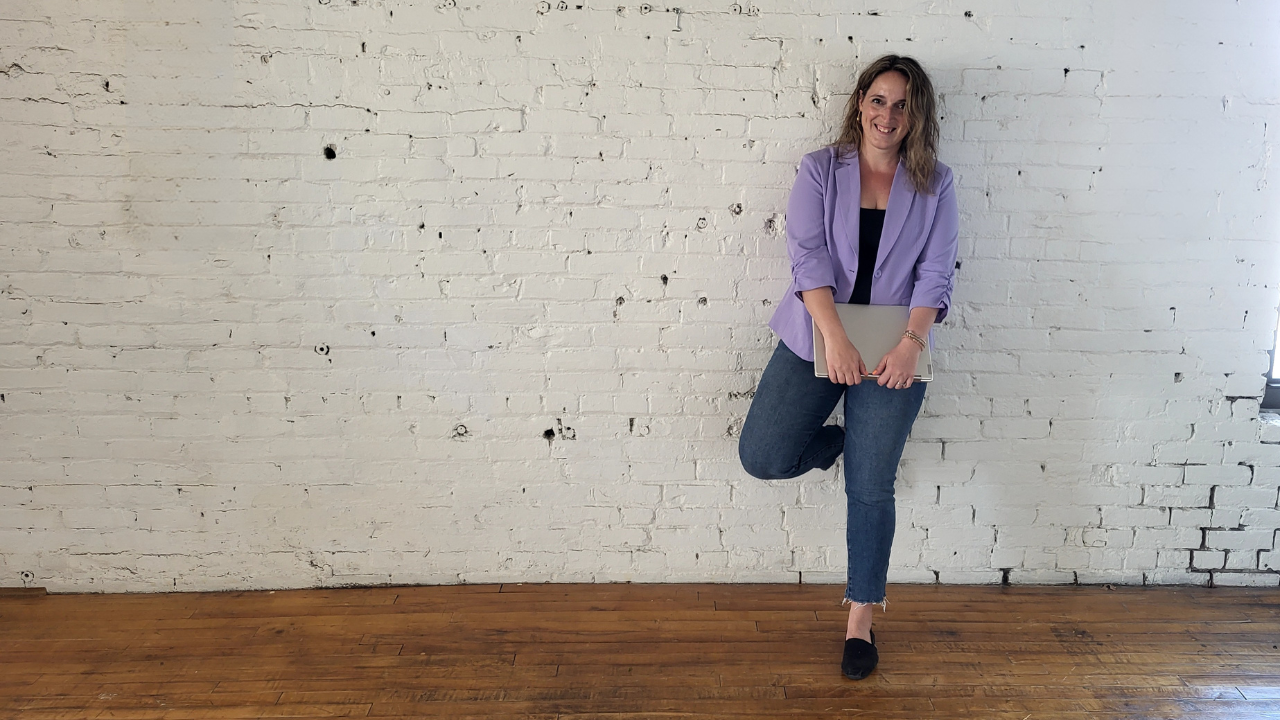 Julie smiling at the camera leaning against the white brick wall